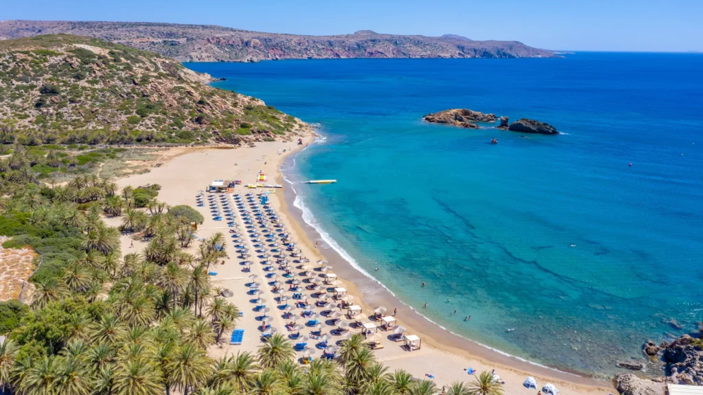Lang zandstrand op Kreta met parasols en turquoise zee in een baai