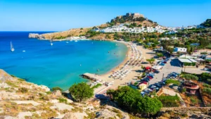 Uitzicht op de baai en het strand bij Lindos op Rhodos, met witte huisjes en de Akropolis op de heuvel.